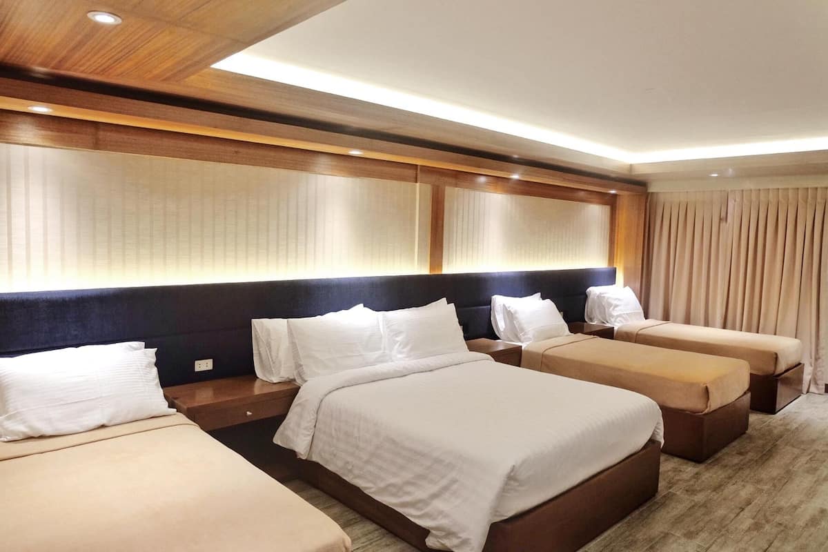 Une chambre d’hôtel avec trois lits, une grande tête de lit et un plafond en bois.