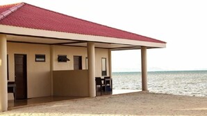 Een gebouw aan het strand met een rood dak, een overdekt zitgedeelte en uitzicht op de zee.