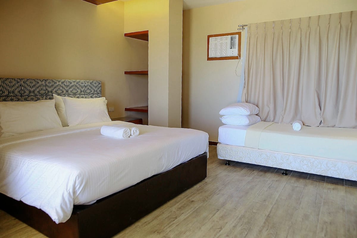 Une chambre d’hôtel avec un grand lit, un petit canapé, une tête de lit en bois et un climatiseur fixé au mur.