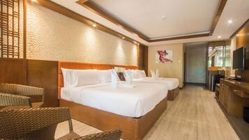 Quarto de hotel com uma cama grande, duas mesas de cabeceira, uma televisão e um espaço de estar com cadeiras de vime.