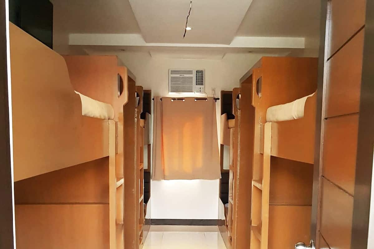 Un couloir bordé de lits superposés de chaque côté, une unité de climatisation centrale et un sol blanc.