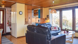 Een gezellig interieur van een blokhut met een houten plafond, een bank, een eettafel en een keukenhoek.
