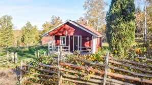 Een rode houten chalet met een veranda, omringd door een houten hek en herfstkleurige bladeren.