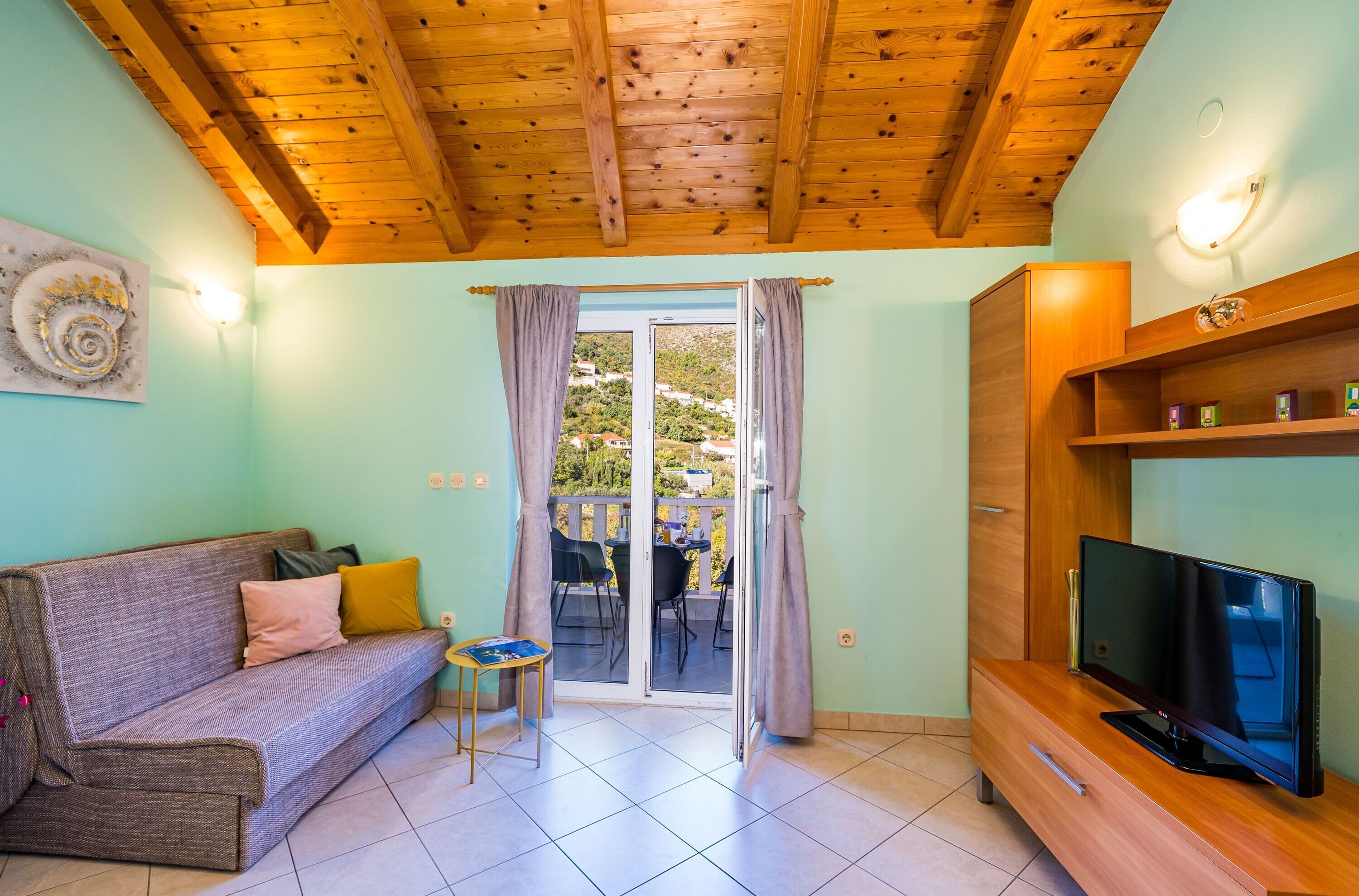Un salon chaleureux avec un plafond en bois, un canapé, un téléviseur posé sur un meuble en bois et une porte-fenêtre coulissante donnant sur un espace extérieur.