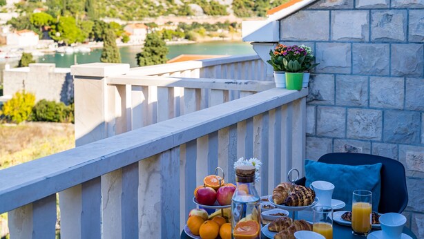 A balcony with a table set for breakfast, including fruits, pastries, and beverages, overlooking a scenic lake and greenery. - Apartments Vodnica - One-Bedroom Apartment with Balcony and Partial Sea View (Zaton Mali)