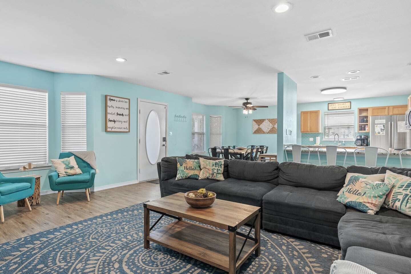 A modern living room with a dark grey sofa, teal armchairs, and a wooden coffee table.