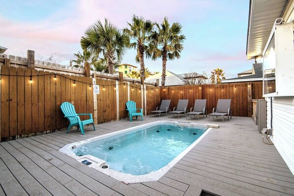 A wooden deck with a hot tub, lounge chairs, and palm trees.