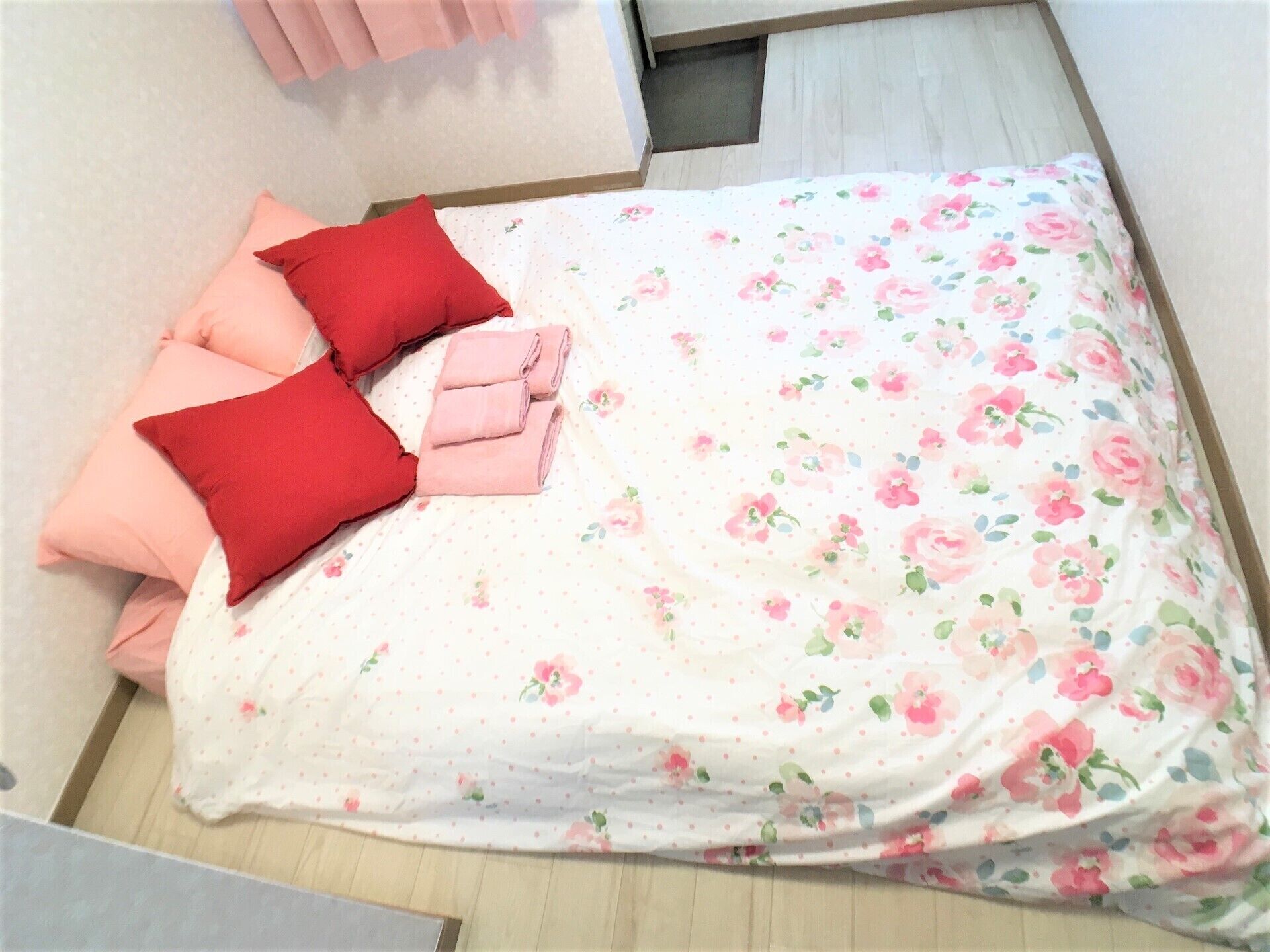 A neatly made bed with floral bedding, pink and red pillows, and a folded blanket.
