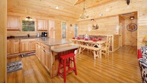 Ein Holzblockhaus-Innenraum mit Küche, Essbereich und einem großen Holztisch.