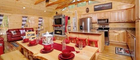 A wooden cabin interior with a dining area, kitchen, and living room.