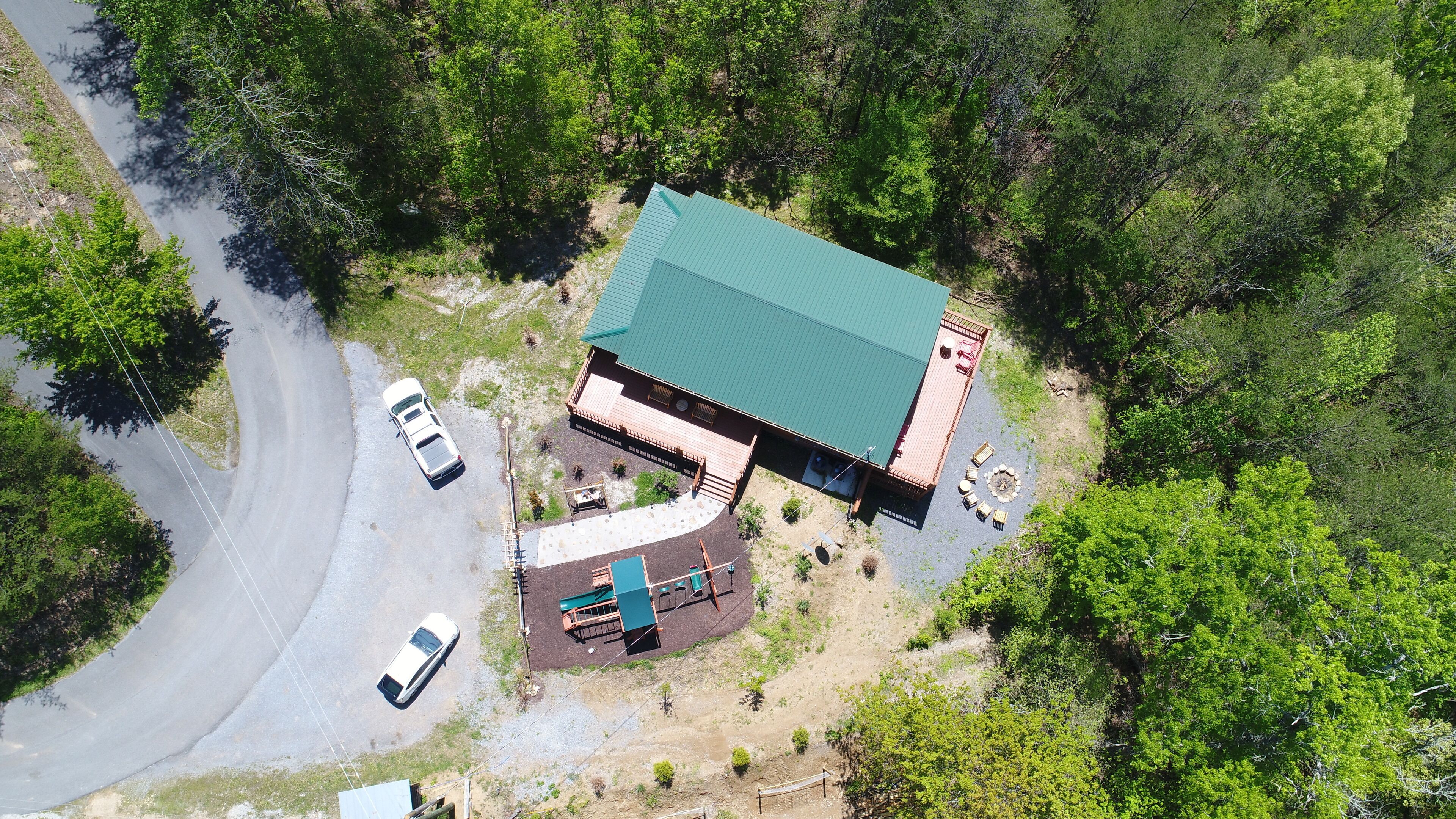 An aerial view of a building with a green roof, surrounded by trees. There are two cars parked in front.