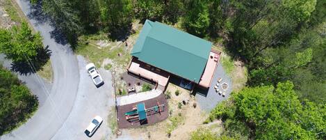 An aerial view of a building with a green roof, surrounded by trees. There are two cars parked in front.