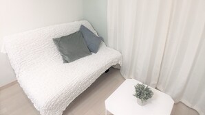 A white textured sofa with a grey and blue pillow, a small white table with a plant, and a white curtain. - Viewcity Shinjukugyoen 801-2 (Tokyo)
