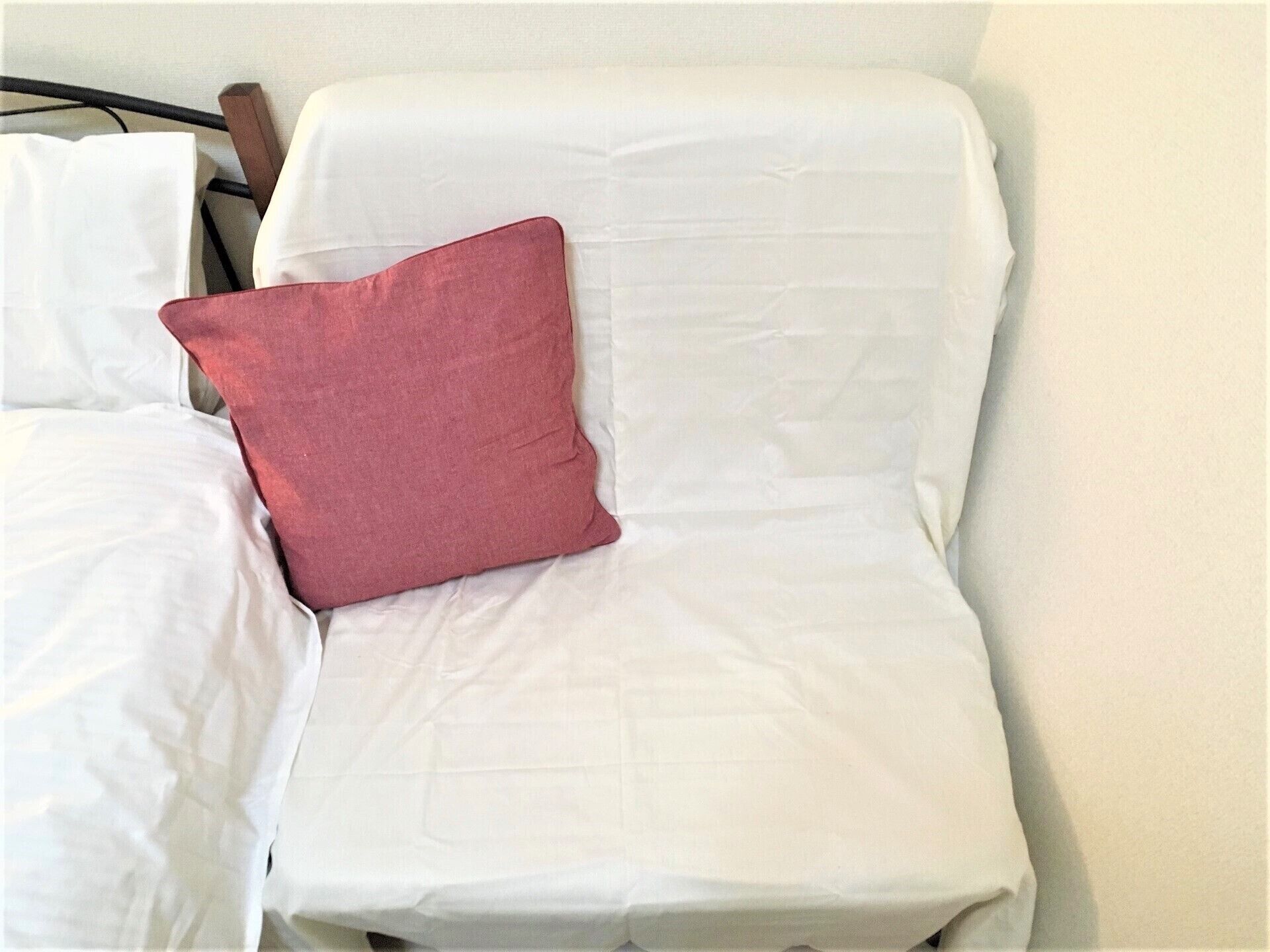 Una cama con ropa de cama blanca y una almohada roja.