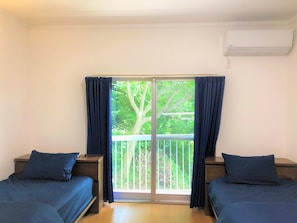 A room with two beds, a sliding glass door leading to a balcony, and an air conditioning unit on the wall. - Vacation House Odawara (Odawara)