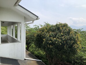 Ein weißes Gebäude mit einem Balkon, der auf einen üppigen grünen Baum und ferne Berge blickt.