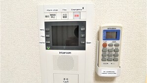 Et intercomsystem ophængt på væggen, med en fjernbetjening ved siden af.