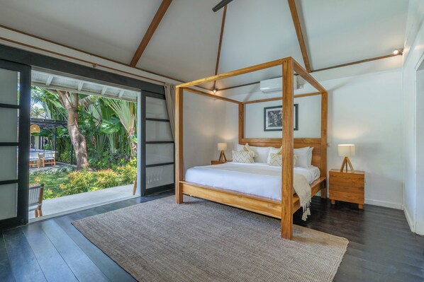 A bedroom with a wooden four-poster bed, a nightstand with a lamp, and a view of a tropical garden through a glass door. - 10 Bdr-Last Minute Deal 50%+ OFF!!! Seminyak (Seminyak)