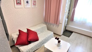 Ein gemütliches Zimmer mit einem weißen Sofa, zwei roten Kissen, einem weißen Tisch mit Blumen und einem grauen Hocker.