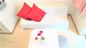 A room with a white sofa, two red pillows, and a small white table with a vase of pink flowers. - Bell Air OKUBO 203 (Tokyo)