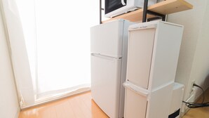Una cocina compacta con un refrigerador blanco, un microondas en un estante y un pequeño contenedor de basura etiquetado como 'Residuos inflamables'.