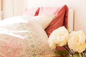 A bed with a patterned blanket and pillows, and two white flowers on a bedside table. - Lions apartment Shinjuku Gyoen 1002 (Tokyo)