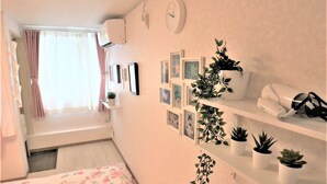 Un dormitorio con cama, una ventana con cortinas, un reloj de pared y varias fotografías enmarcadas.