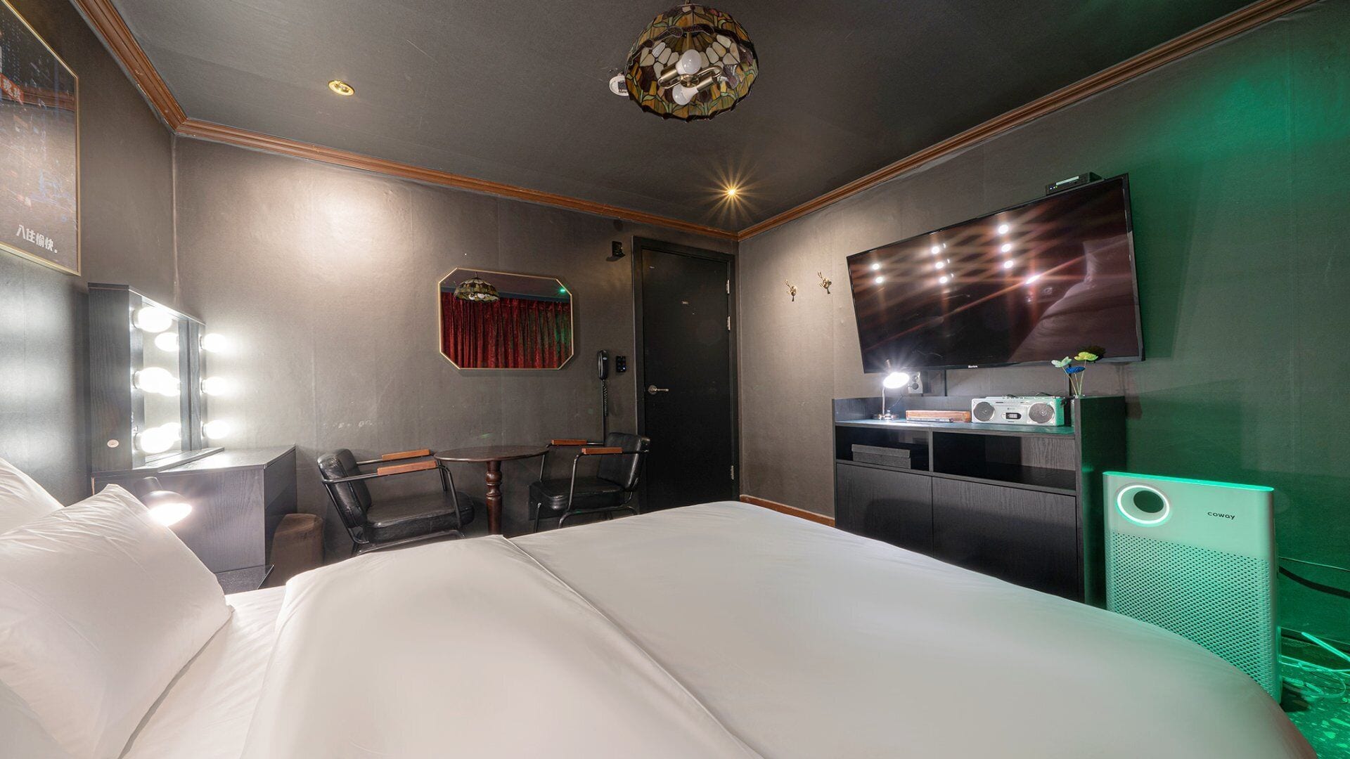 Une chambre d’hôtel avec un grand lit, un bureau avec un ordinateur, une télévision et un miroir avec éclairage intégré.