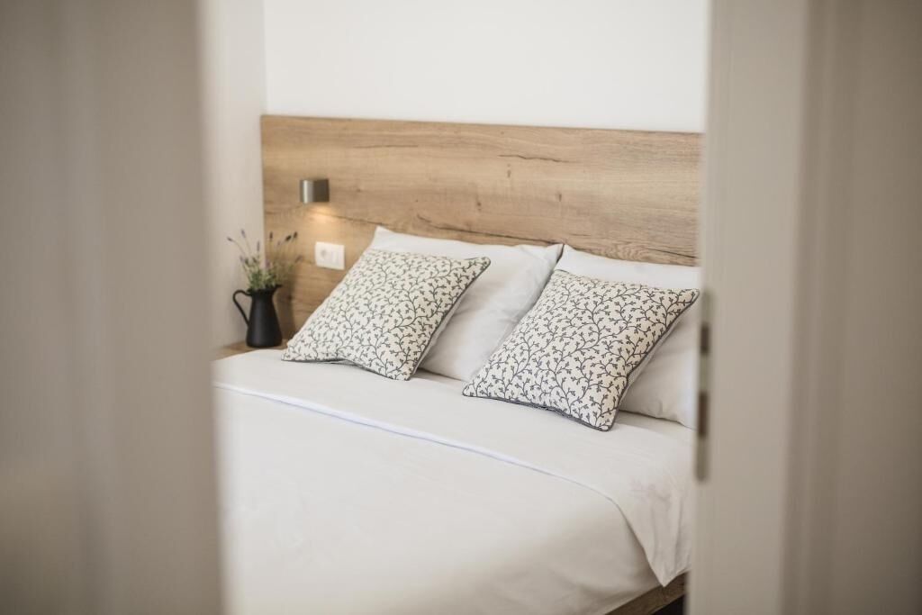 A bed with a wooden headboard, two pillows with a floral pattern, and a bedside table with a small potted plant.