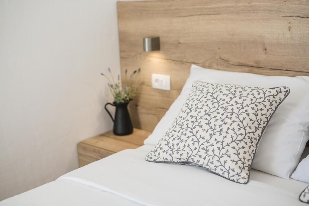 Un lit bien fait, avec un drap blanc et un coussin décoratif orné d’un motif floral.