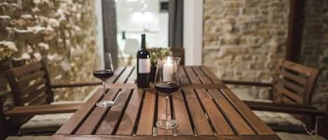 A wooden table with two wine glasses and a bottle, set against a stone wall.