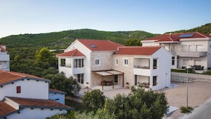A modern two-story house with a stone facade, a red-tiled roof, and a covered outdoor seating area.