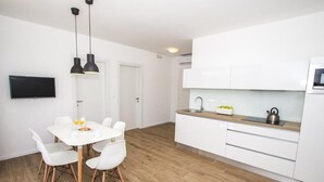 A modern kitchen with white cabinets, a wooden countertop, and a kettle. There is a dining area with a white table and chairs.