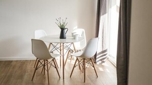 A modern dining area with a round table, white chairs, a black vase with flowers, and a black pendant light.