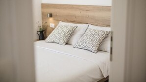 A bed with a wooden headboard, two pillows with a floral pattern, and a bedside table with a small potted plant.