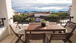 A wooden table with four chairs on a balcony, a potted plant, and a glass of water.
