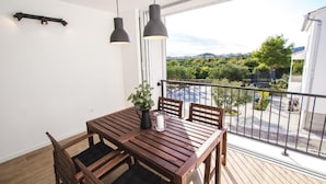 Un balcón con mesa y sillas de madera, una planta en maceta y vistas a zonas verdes y edificios.