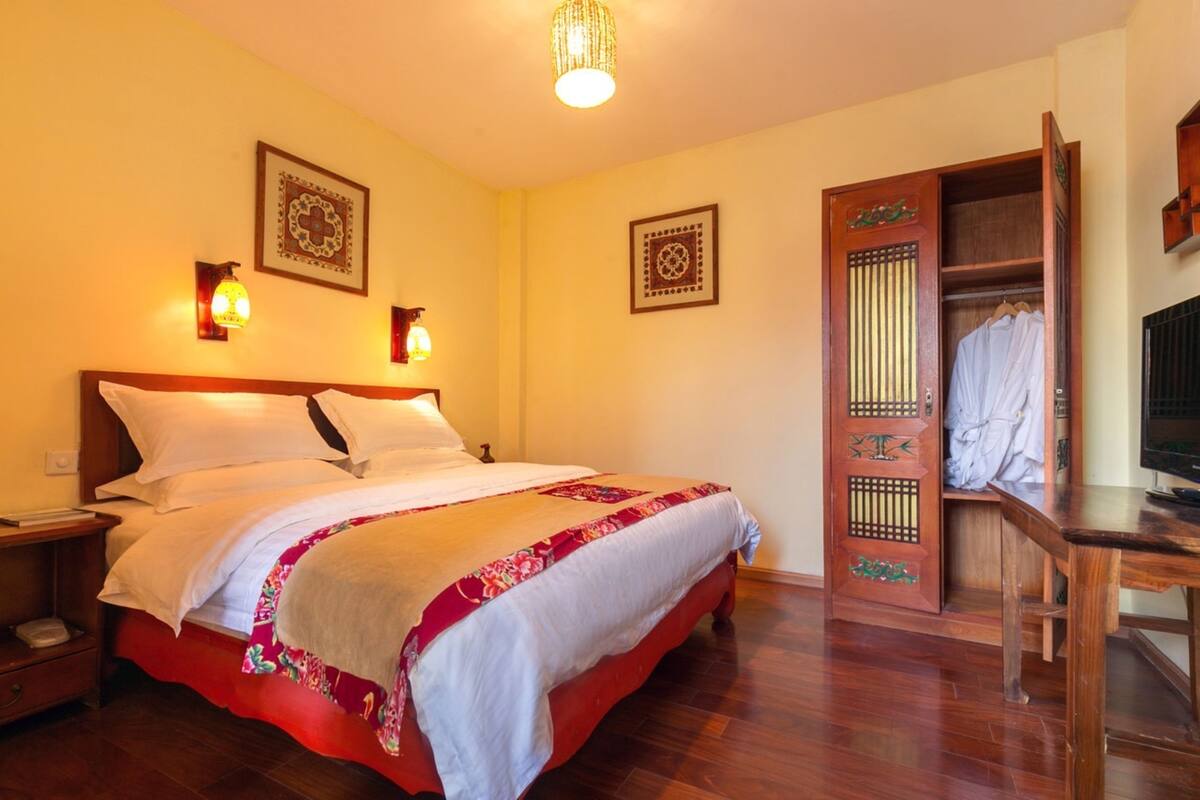 A neatly made bed with a wooden headboard, a bedside table with a lamp, and a wardrobe with a traditional design.
