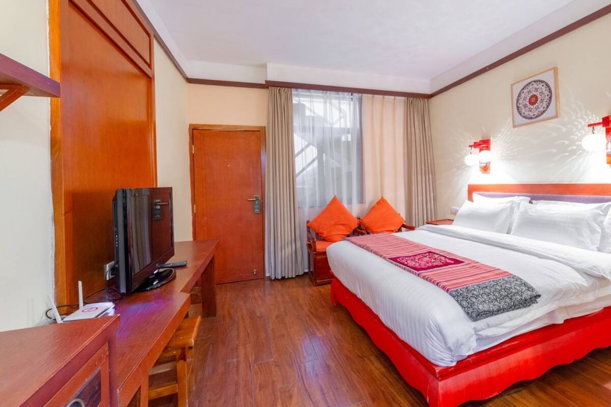 A hotel room with a large bed, wooden furniture, a television, and a window with curtains.