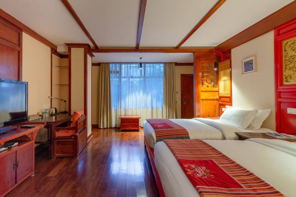 A hotel room with a TV, wooden furniture, a bed with a red blanket, and a window with curtains.