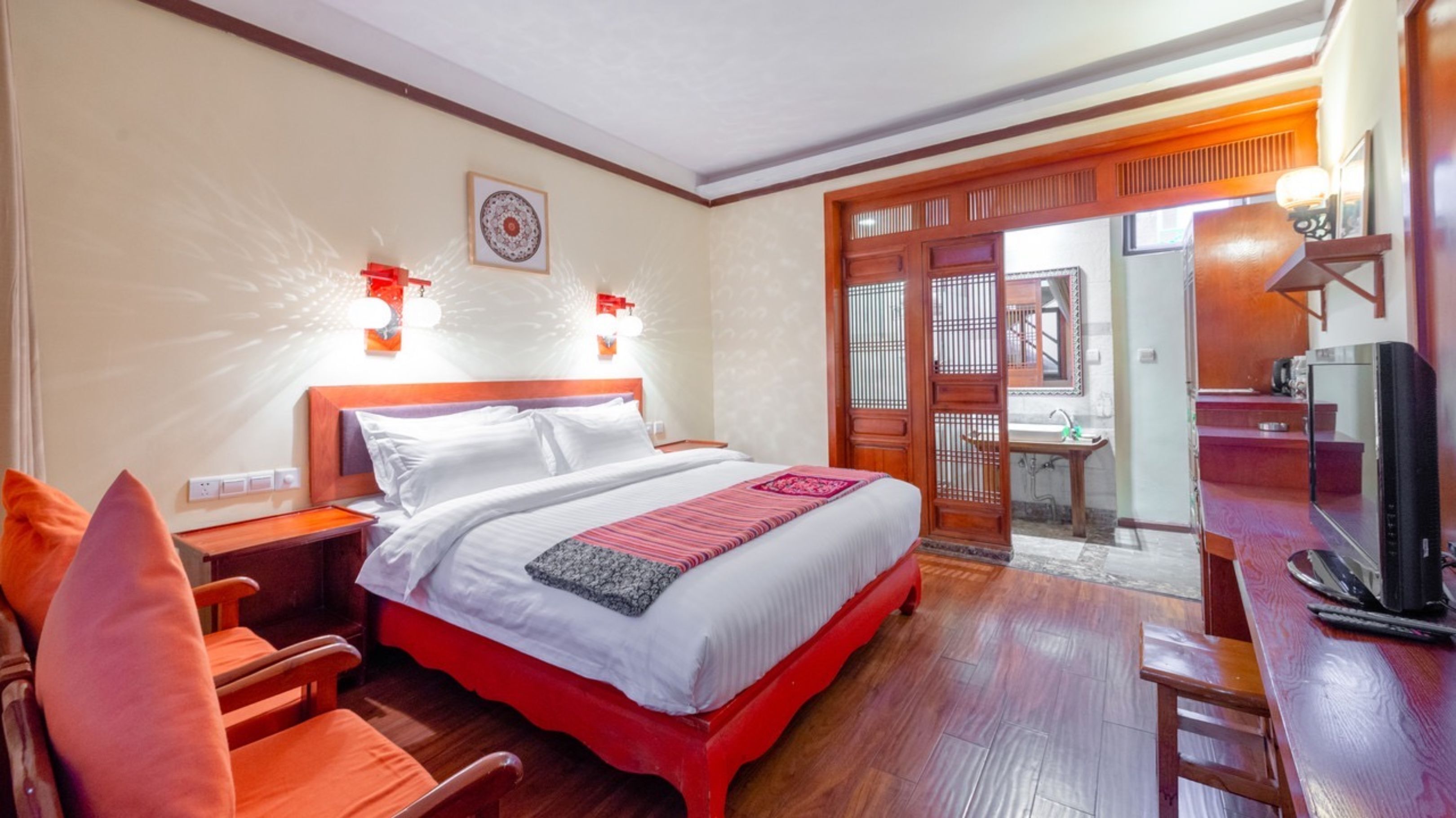 A hotel room with a bed, a chair, a desk with a television, and a bathroom visible through an open door.