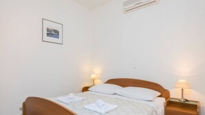 En pænt redt seng med hvide sengetæppe og håndklæder, en træsenggavl, et natbord med en lampe og et billedramme på væggen.