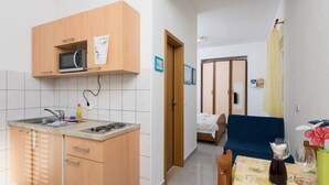 A compact kitchen with a microwave, sink, and wooden cabinets. A dining area with a table and chairs is visible, featuring a vase and a bottle. - Studio apartment in Orebić with Terrace, Air condition, WIFI (4934-2) (Orebic)
