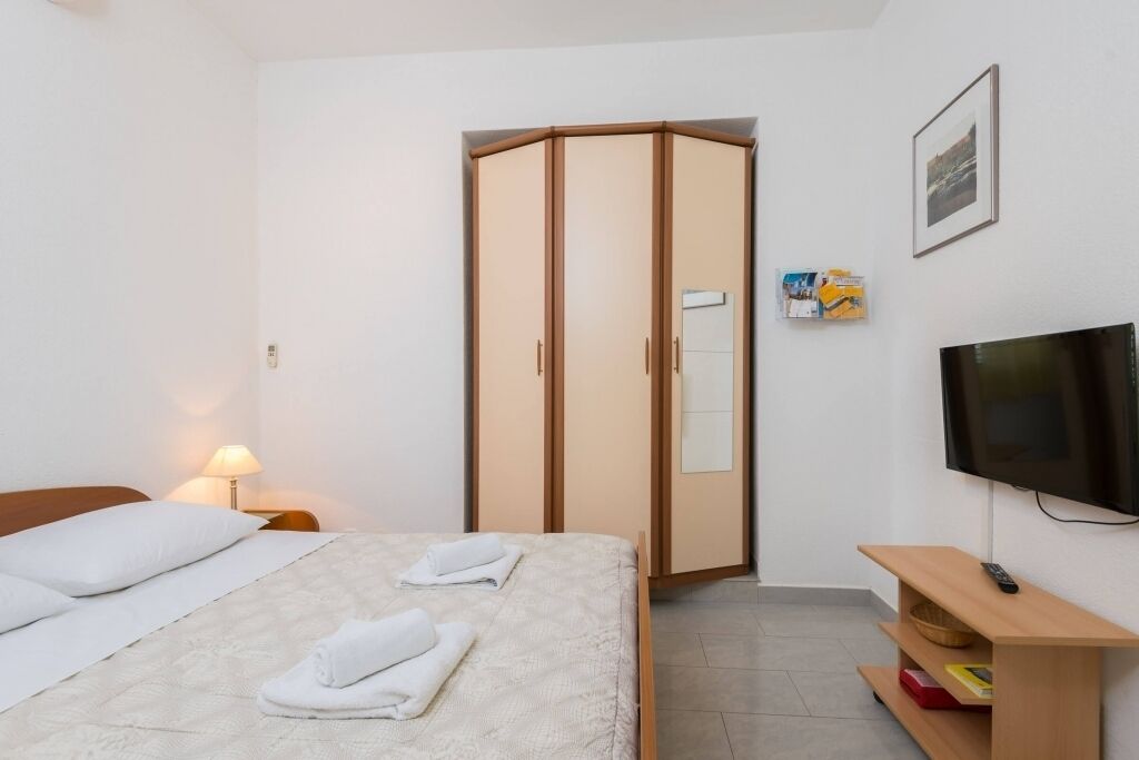 Une chambre d’hôtel comprenant un lit, une armoire, une télévision et une table de chevet avec une lampe.