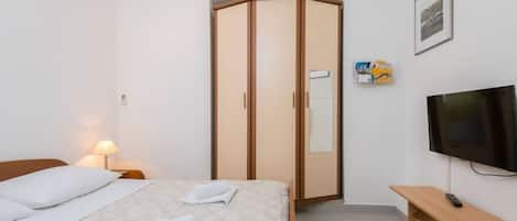 Ein Hotelzimmer mit einem Bett, einem Kleiderschrank, einem Fernseher und einem Nachttisch mit Lampe.