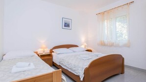 Un dormitorio con dos camas individuales, cabecero de madera, lámparas de noche, un cuadro enmarcado en la pared y una ventana con cortinas de encaje.