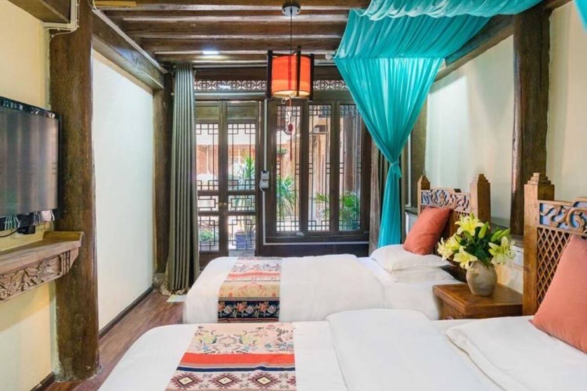 A hotel room with two beds, a TV, a window with curtains, and a view of the outside.