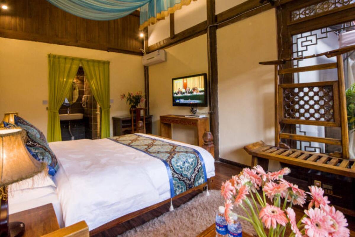 A hotel room with a bed, a TV, a wooden chair, a table with water bottles and flowers, and a decorative screen.