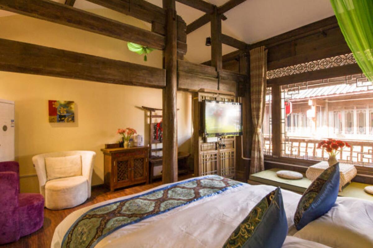 A room with a bed, a chair, a television, and a window with curtains.