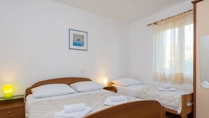A hotel room with two beds, a bedside table with a lamp, a window with sheer curtains, and a framed picture on the wall. - Apartment in Orebić with Balcony, Air condition, WIFI, Dishwasher (4934-6) (Orebic)